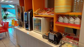 A breakfast bar with various food items, a coffee machine, a toaster, and a refrigerator.