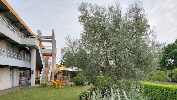 A courtyard with a staircase, outdoor seating, and a large tree. - Premiere Classe Saintes (Saintes)
