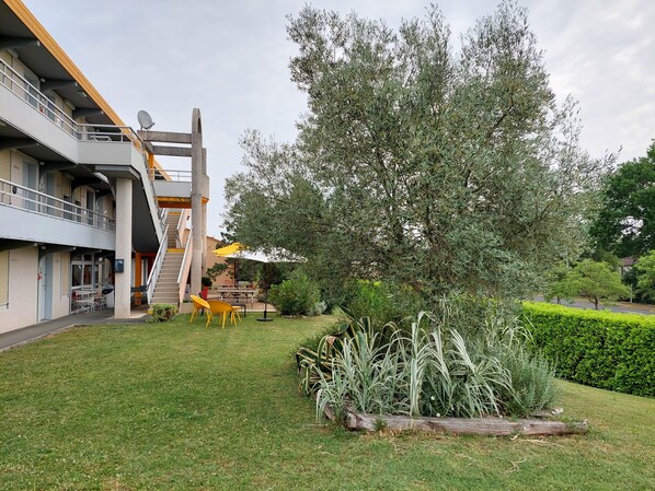 A courtyard with a staircase, outdoor seating, and a large tree. - Premiere Classe Saintes (Saintes)
