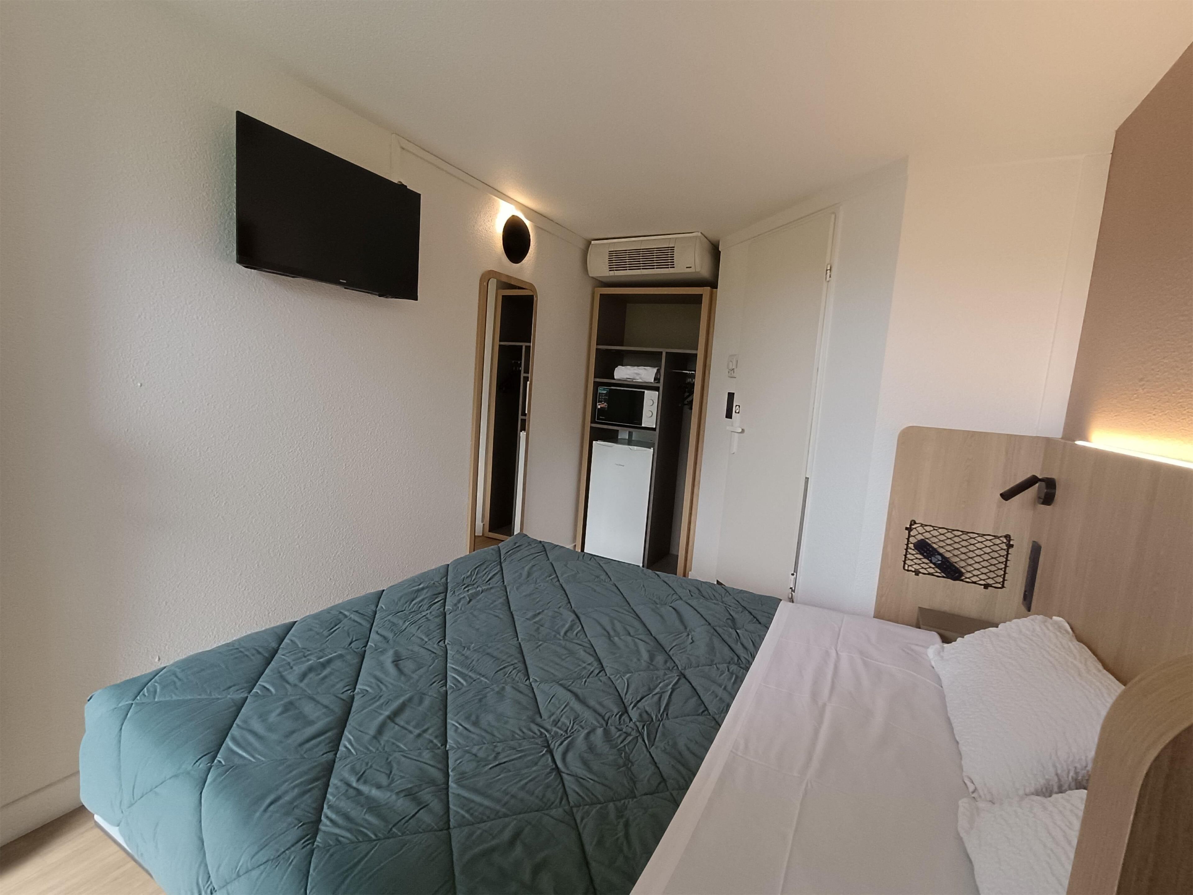 A bedroom with a bed, a TV mounted on the wall, and a wardrobe with a mirror.
