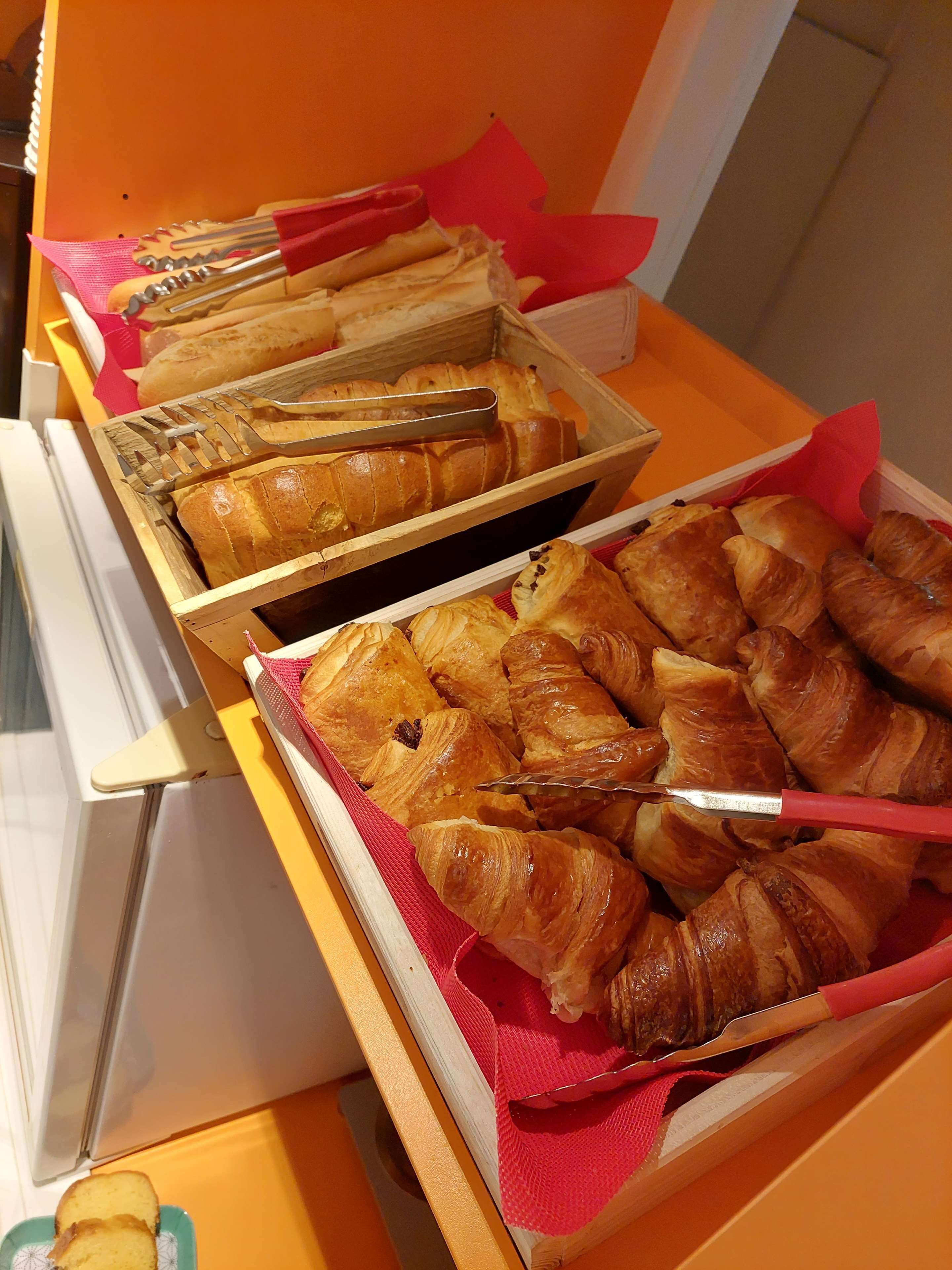 Un bufé con diversas opciones de panadería, incluyendo pan y croissants, dispuestas sobre tablas de madera con servilletas rojas.