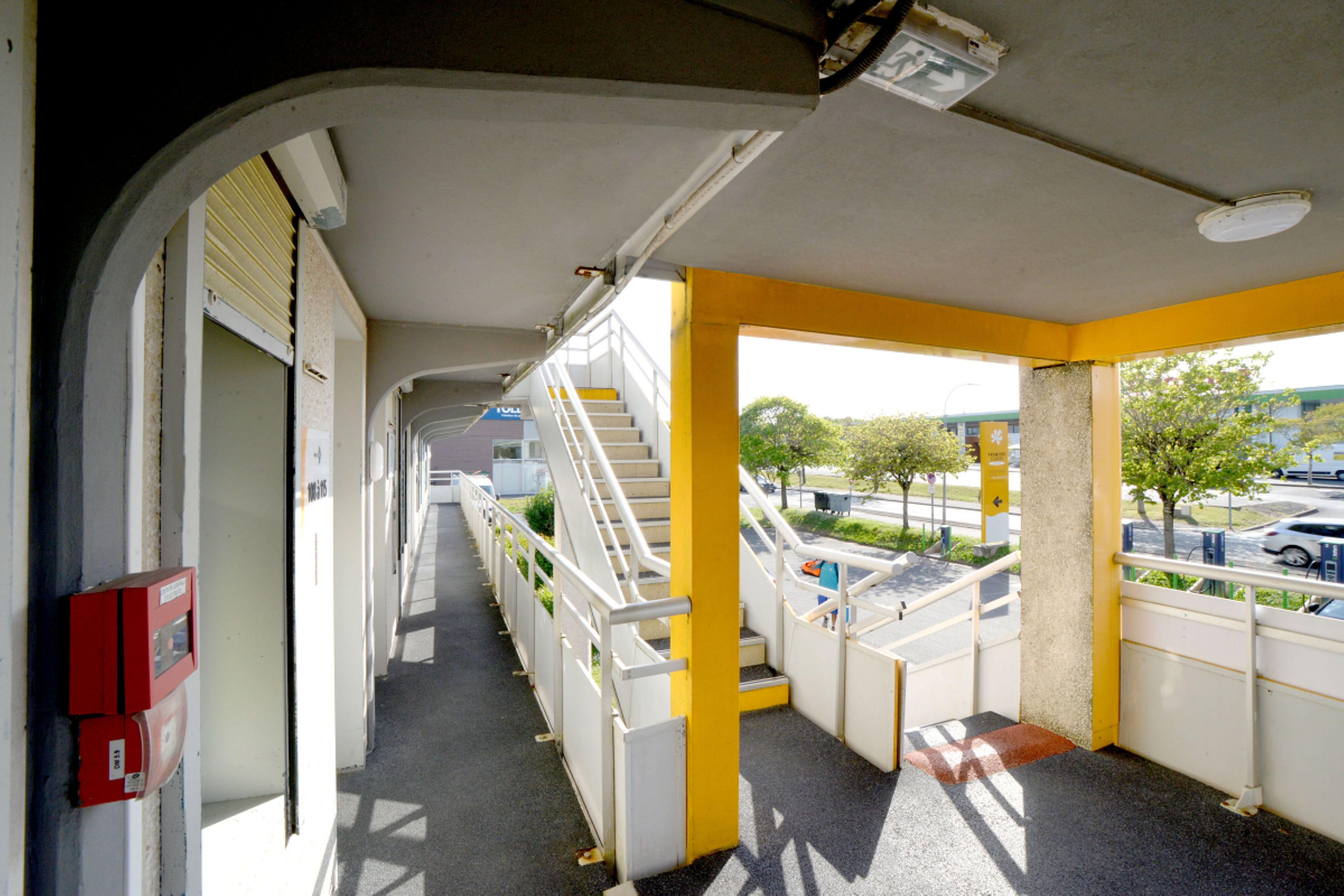 A corridor with a view of a parking area and a building in the distance.
