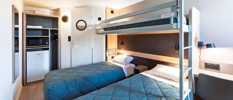 A compact room with a bunk bed, a desk, a microwave, and a refrigerator.