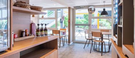Interior moderno de una cafetería con mobiliario de madera, una barra con aderezos y grandes ventanales con vistas al exterior.