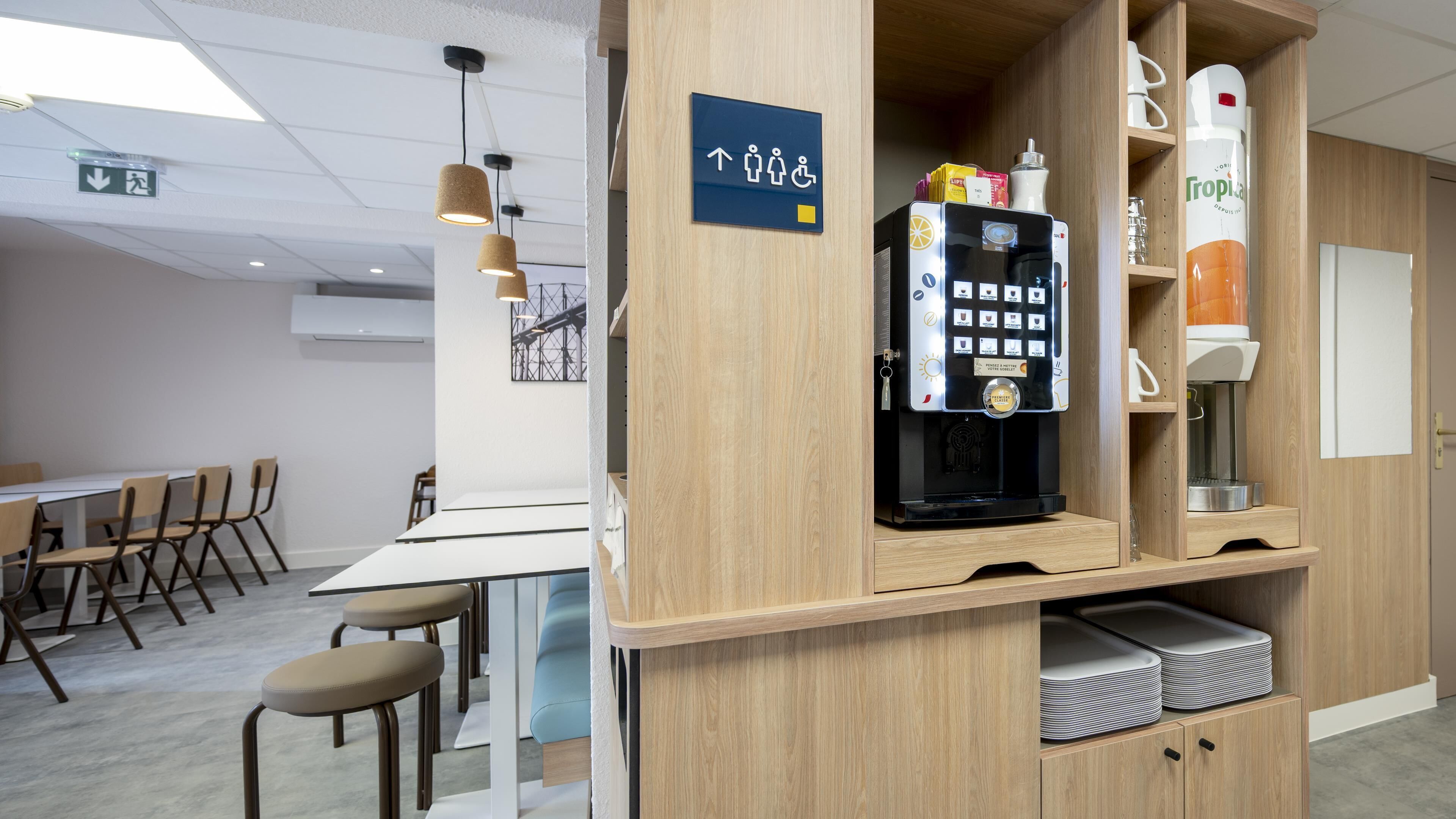 A modern cafe with a coffee machine, seating area, and a sign indicating facilities.
