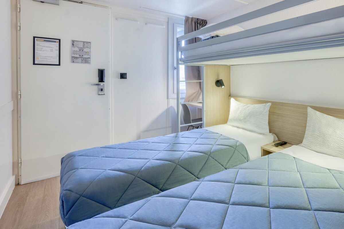 Un dormitorio con literas, una mesita de noche con un control remoto y una puerta con letrero de seguridad.