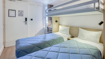Un dormitorio con literas, una mesita de noche con un control remoto y una puerta con letrero de seguridad.