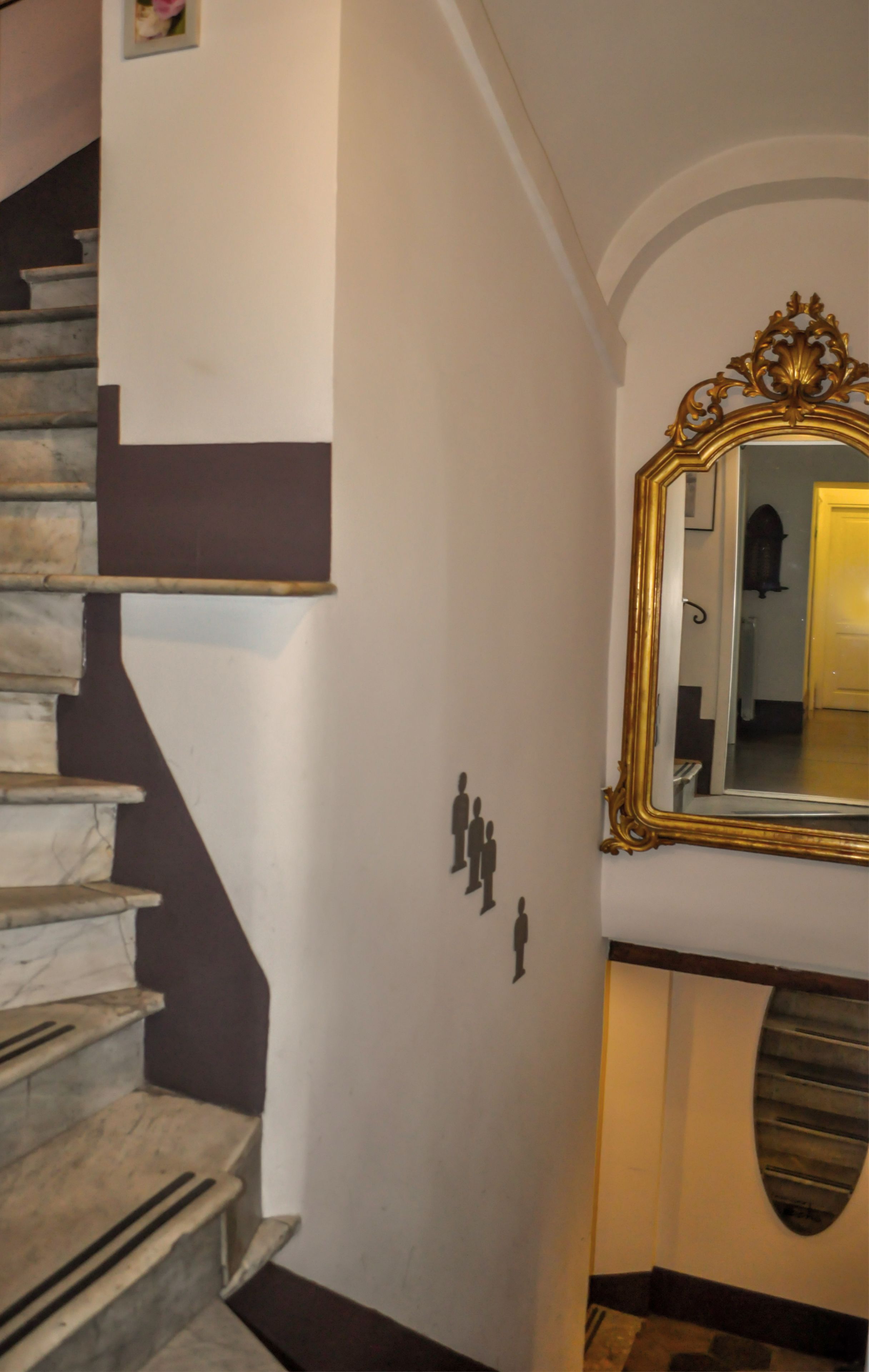 A staircase with a marble finish, a wall-mounted mirror with an ornate gold frame, and a small decorative sculpture of figures.