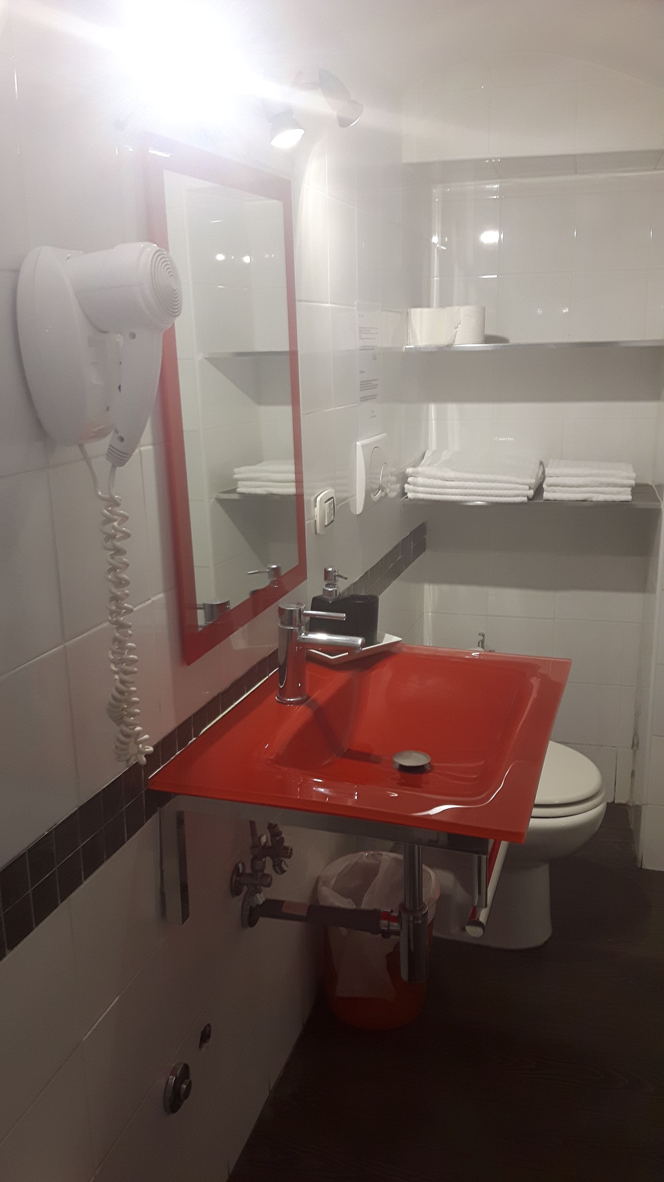 A bathroom with a red sink, white toilet, and a mirror.
