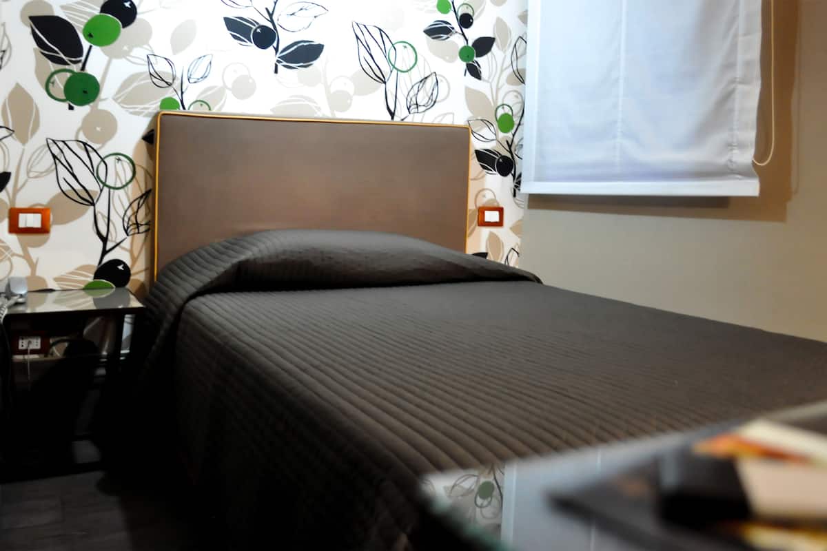 A neatly made bed with a headboard, a bedside table with a lamp, and a wall with a leaf pattern.