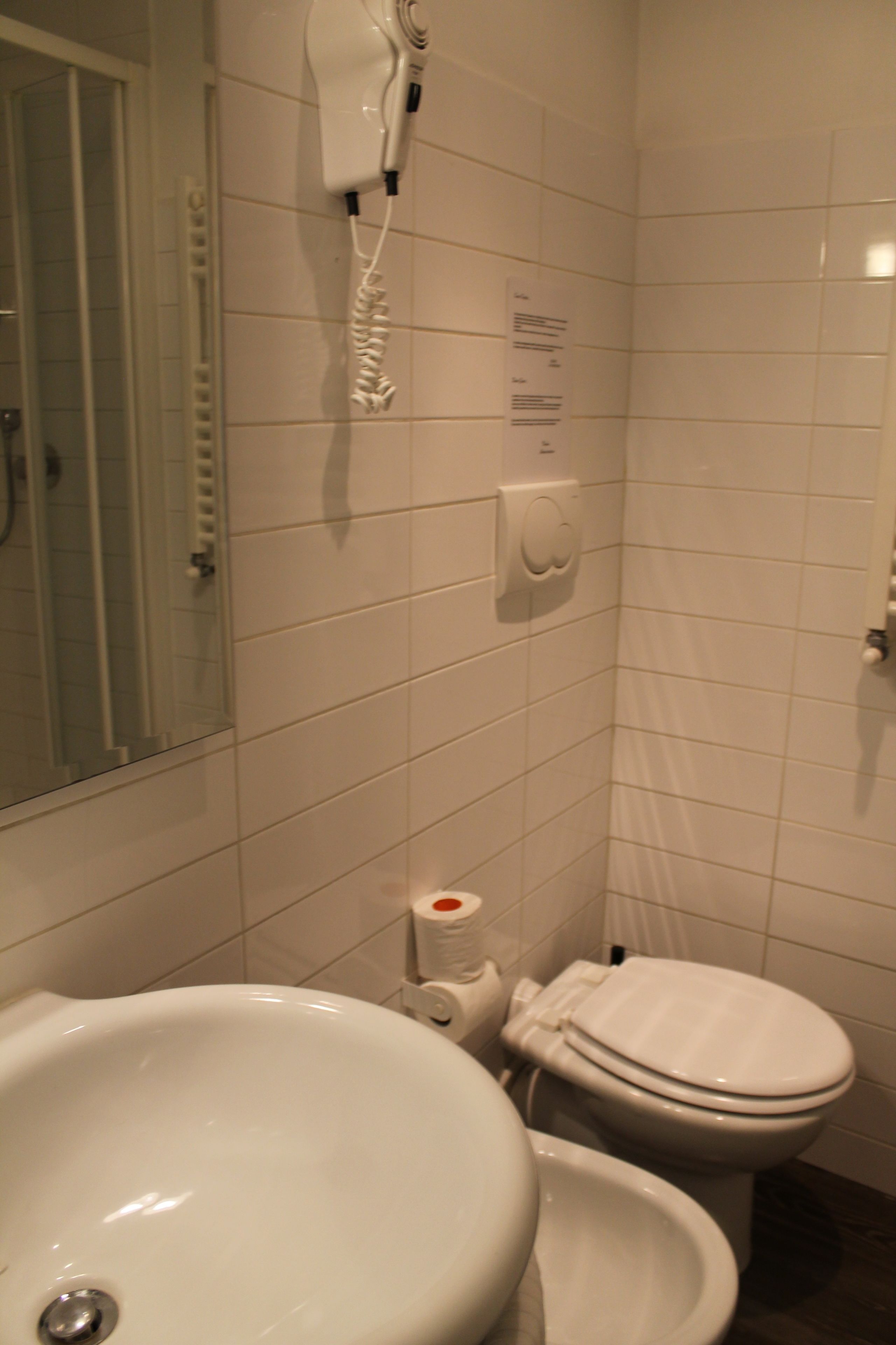 A bathroom with a sink, toilet, and a hairdryer mounted on the wall.