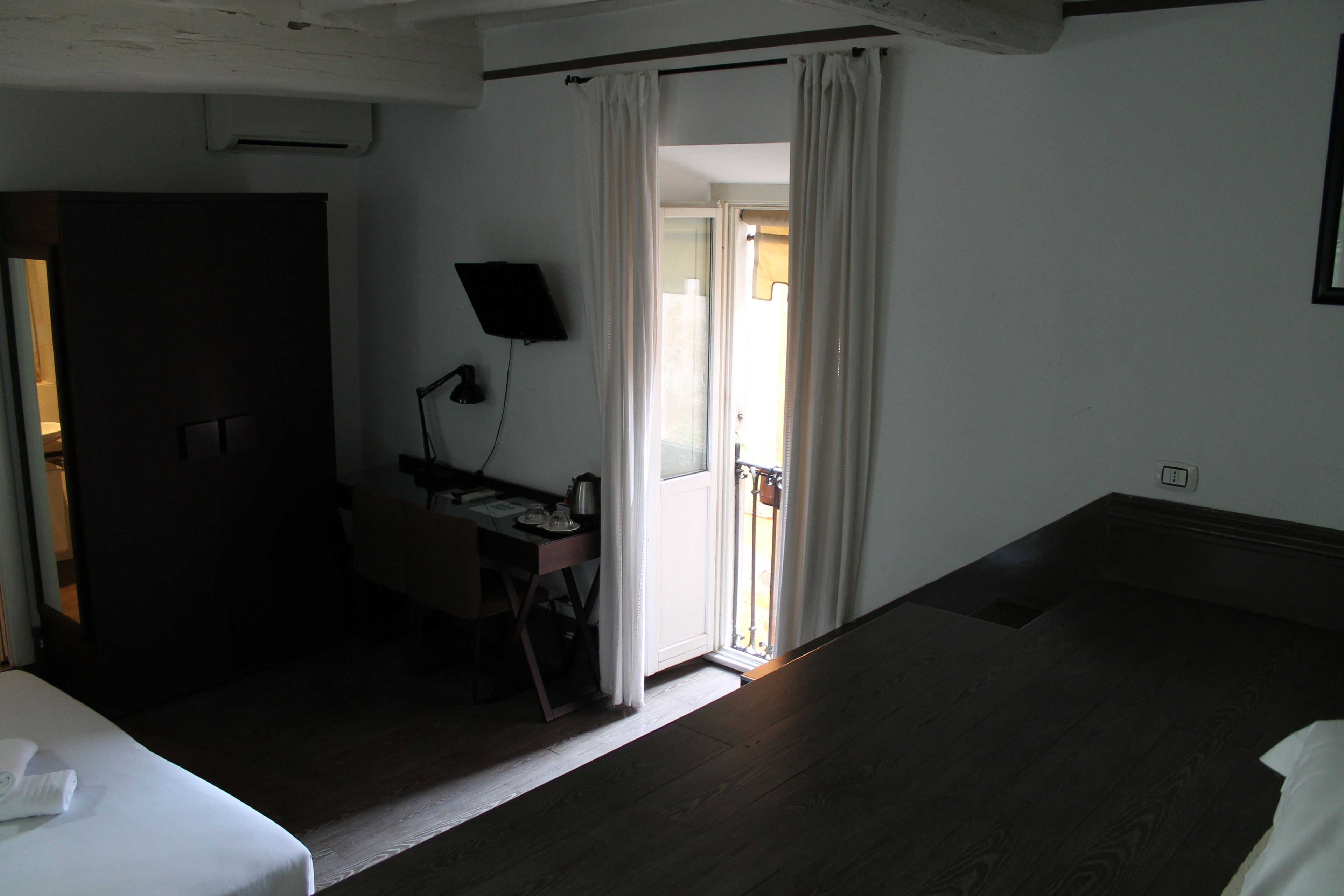 A hotel room with a bed, a desk with a chair, a TV, and a door leading to a balcony.