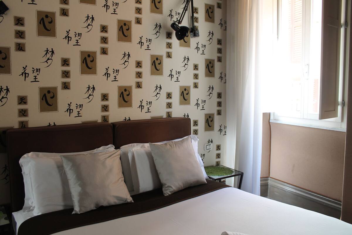A hotel room with a bed, pillows, a nightstand, and a wall with Chinese characters.
