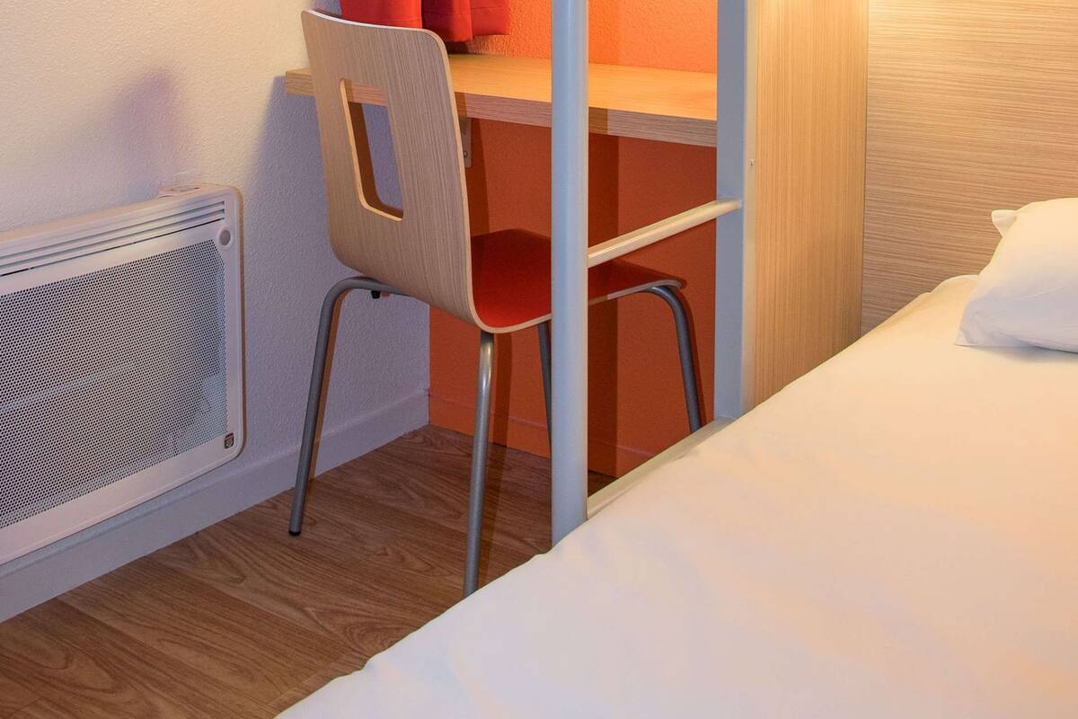 Un lit superposé avec un bureau et une chaise, une fenêtre avec des rideaux rouges et une lampe fixée au mur.