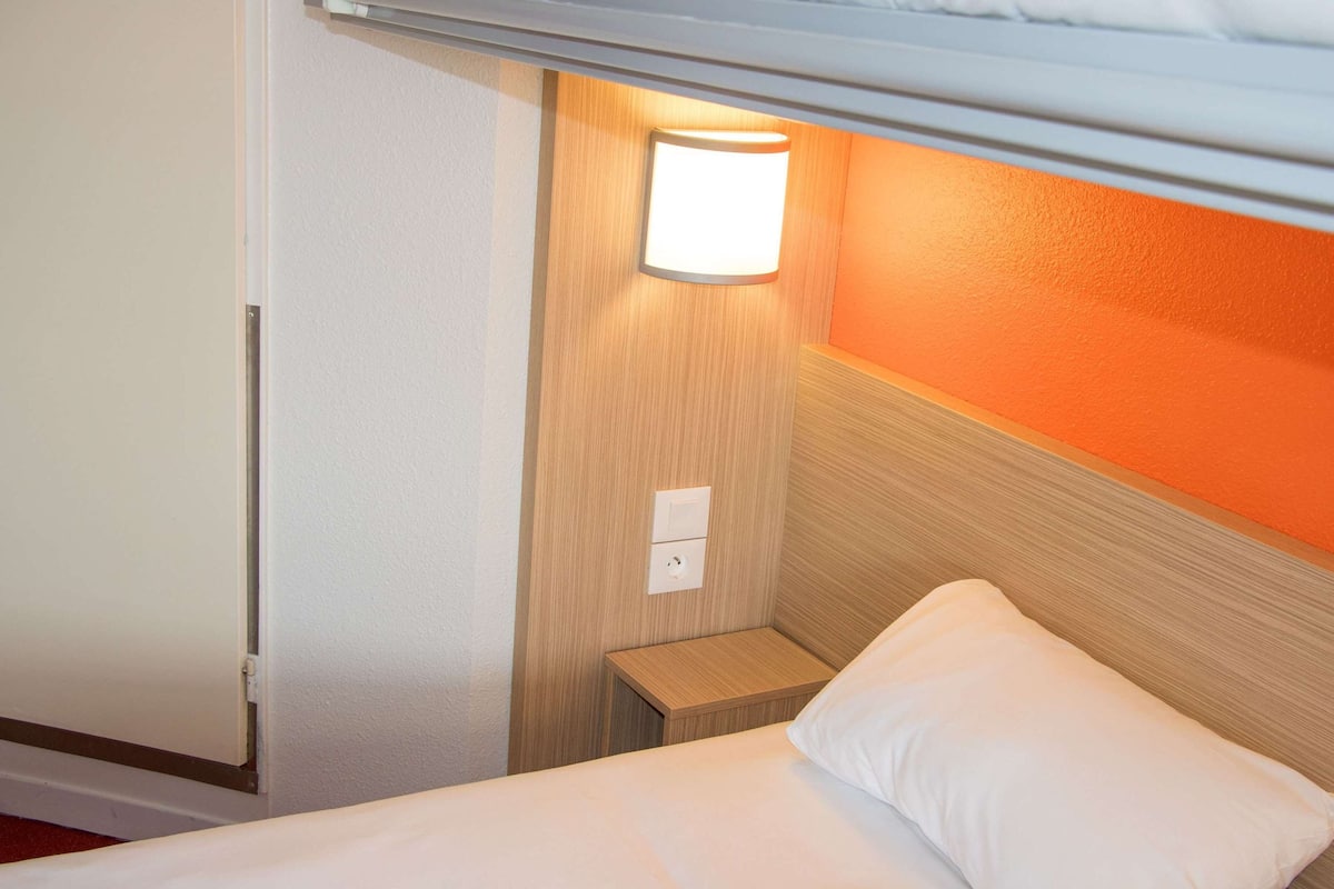 Une chambre d’hôtel avec un lit superposé, une table de chevet avec une lampe et une petite commode.