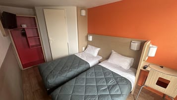 Ein Hotelzimmer mit zwei Betten, einem Kleiderschrank, einem Schreibtisch mit Lampe sowie einem Fernseher.
