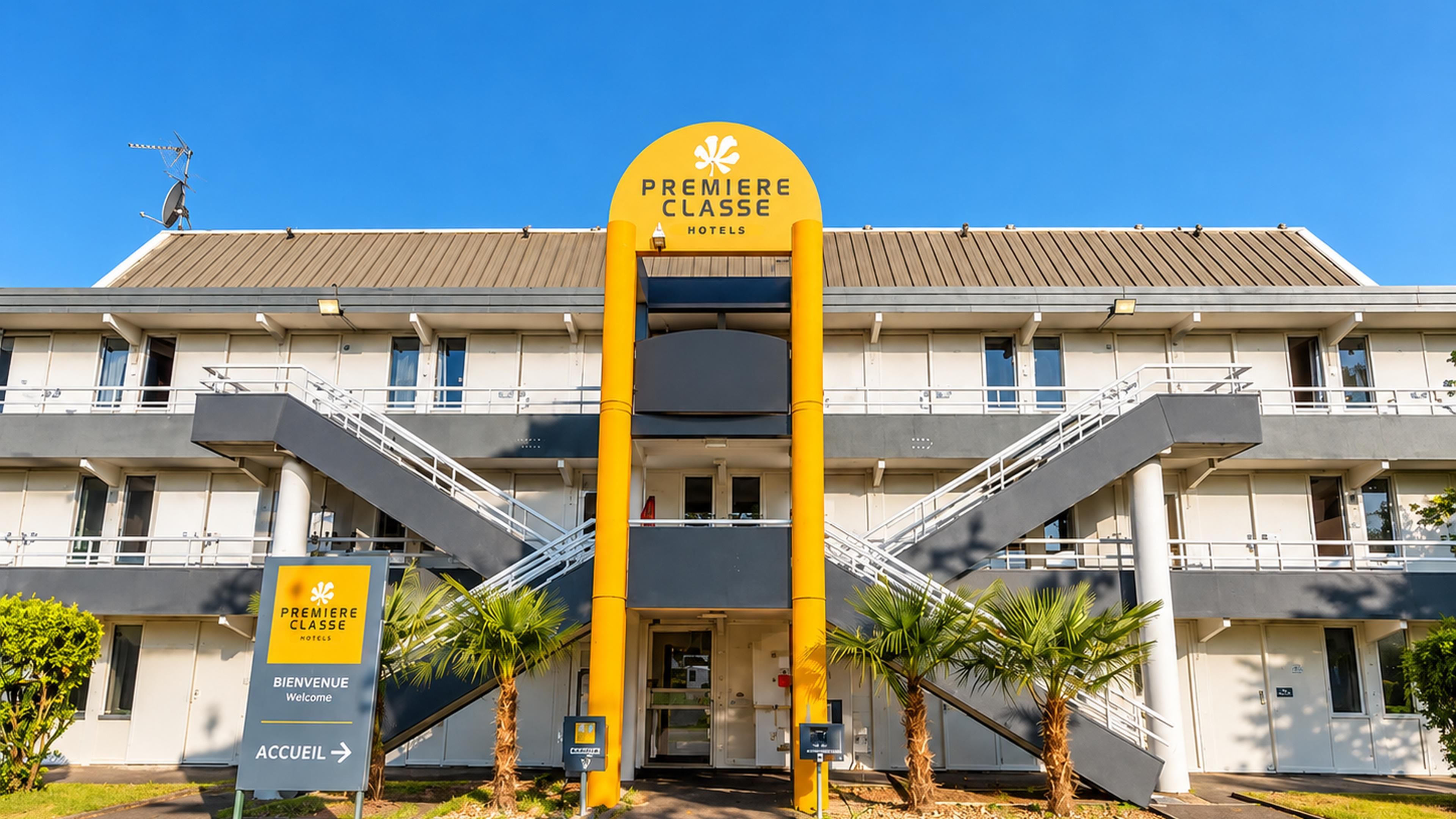 Entrada de hotel con un llamativo letrero amarillo, una escalera y una palmera en primer plano.