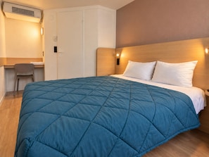 A hotel room with a bed, a desk, and a chair.