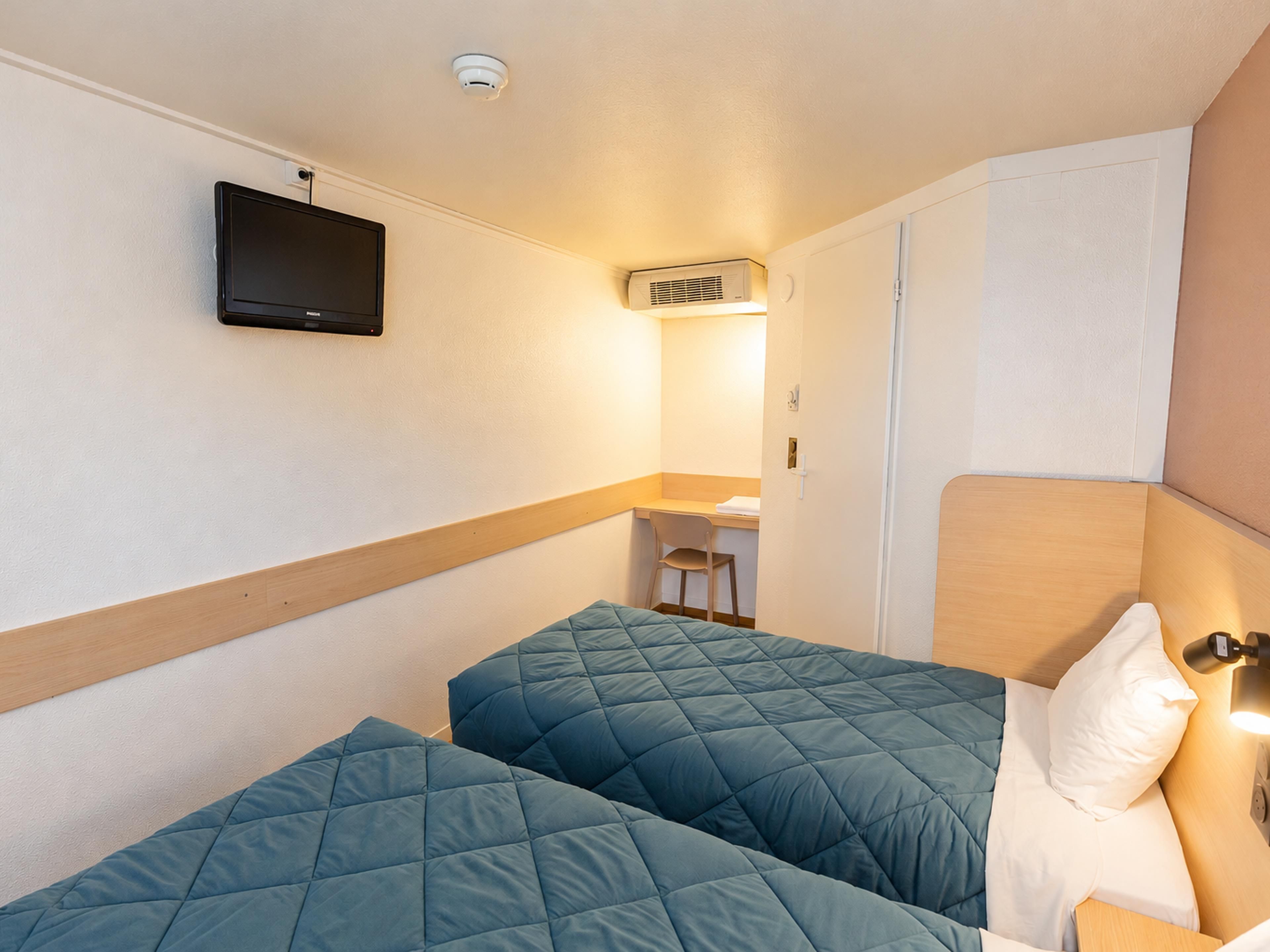 Una habitación de hotel con dos camas, un escritorio y una televisión fijada en la pared.