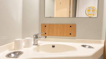 Un baño con un lavamanos blanco, dos grifos y un espejo encima.