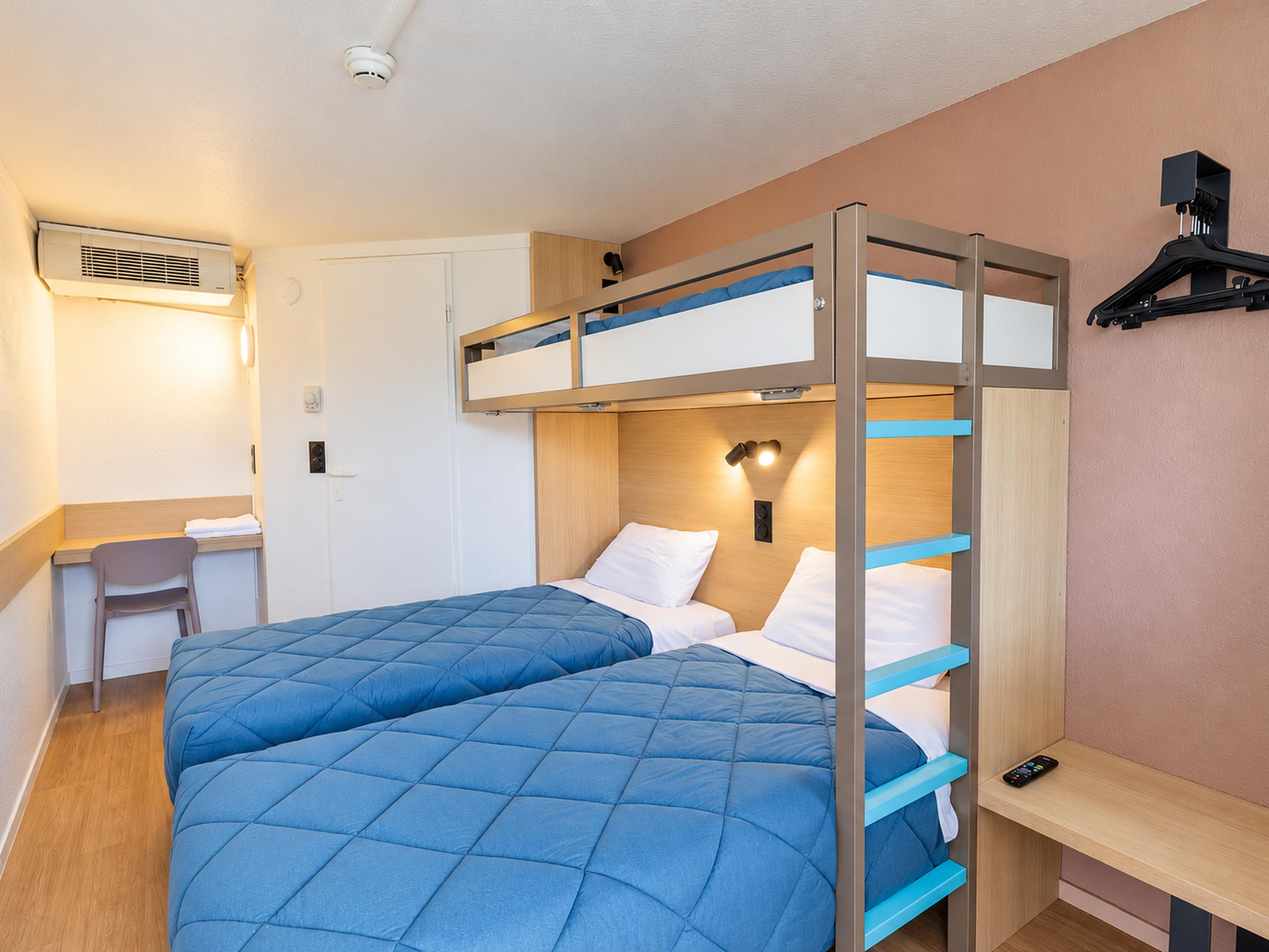 A bunk bed room with a desk and chair, a wall-mounted light, and an air conditioning unit.