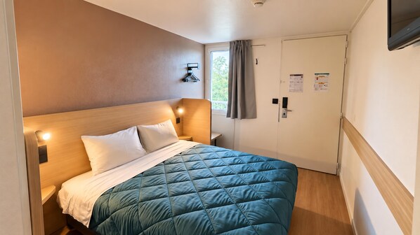 Habitación de hotel con cama, mesita de noche, luz de pared y una puerta con ventanal.