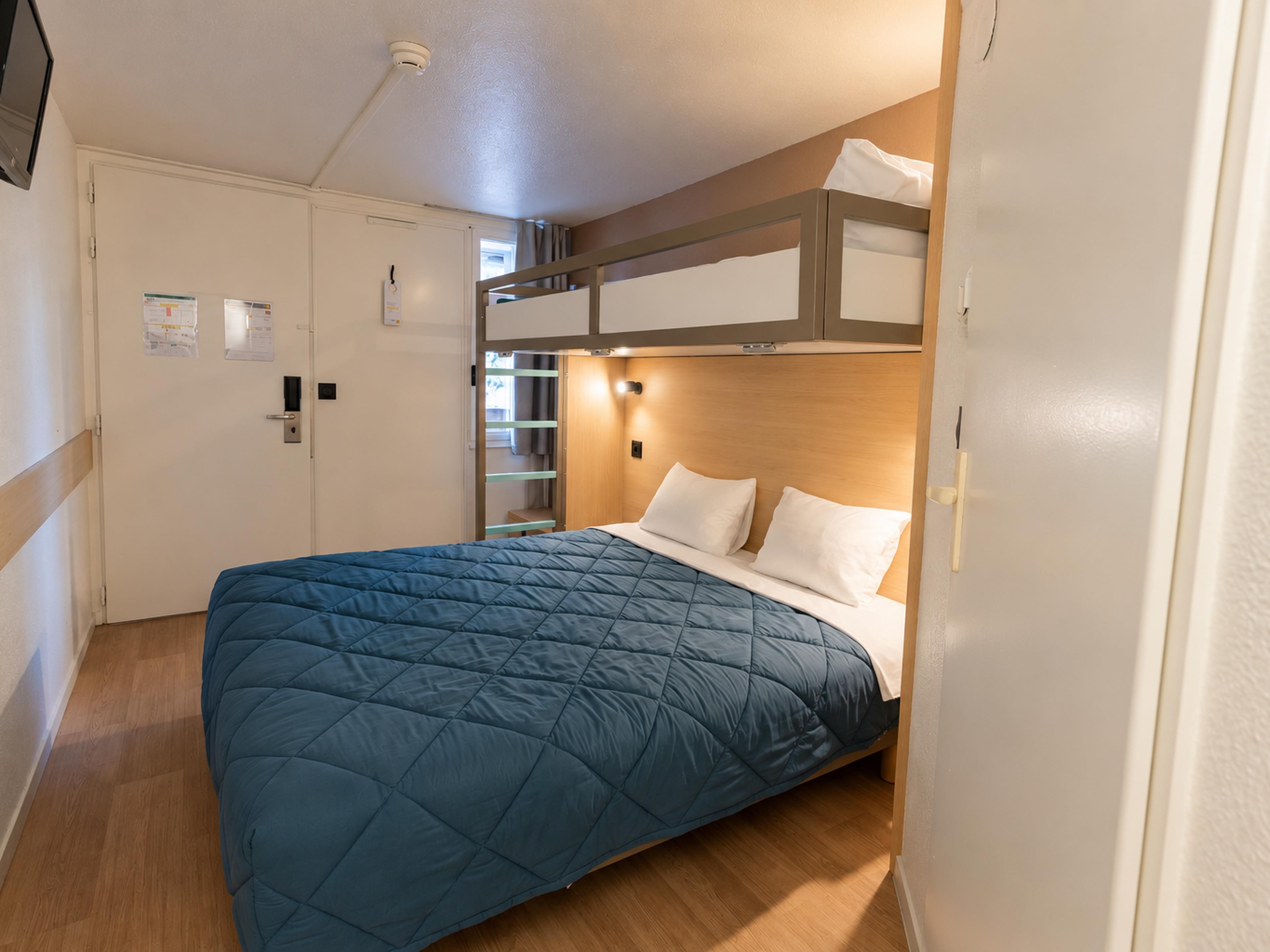 A room with a bunk bed, a single bed with a blue quilt, a wooden headboard, a white door, and a small window.