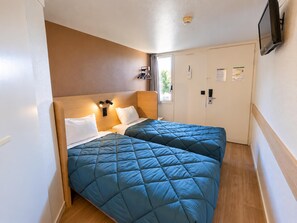 A hotel room with two beds, a wooden headboard, a flat-screen TV mounted on the wall, and a door with a handle.