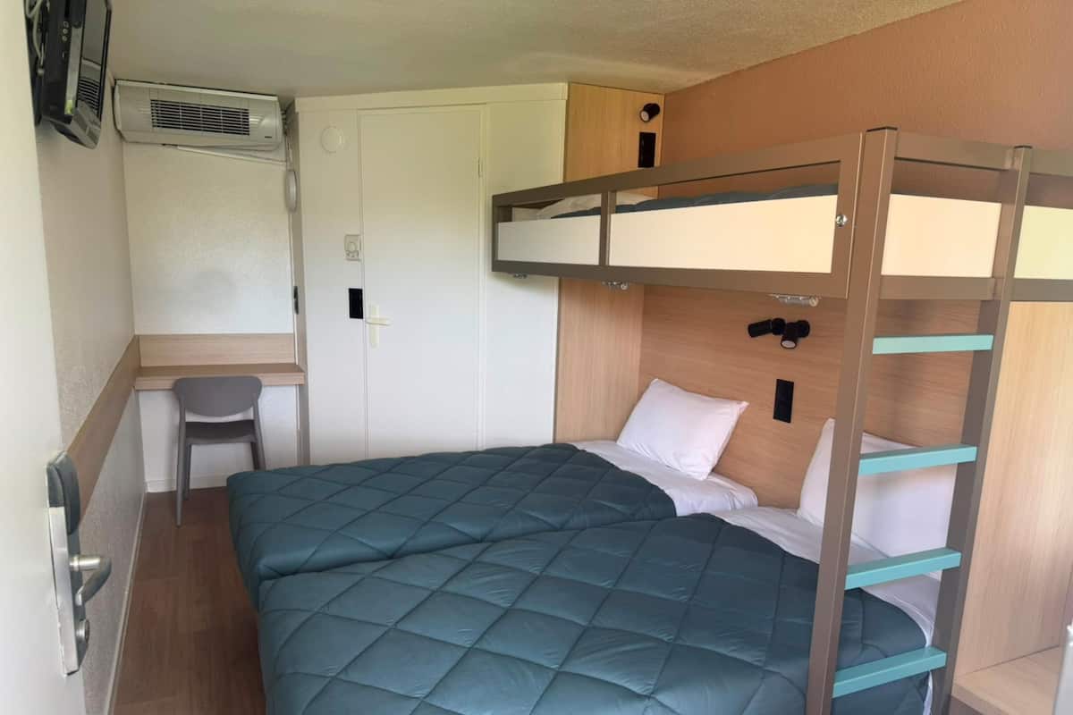 A bunk bed with a quilted mattress, a desk with a chair, and a wall-mounted air conditioning unit.