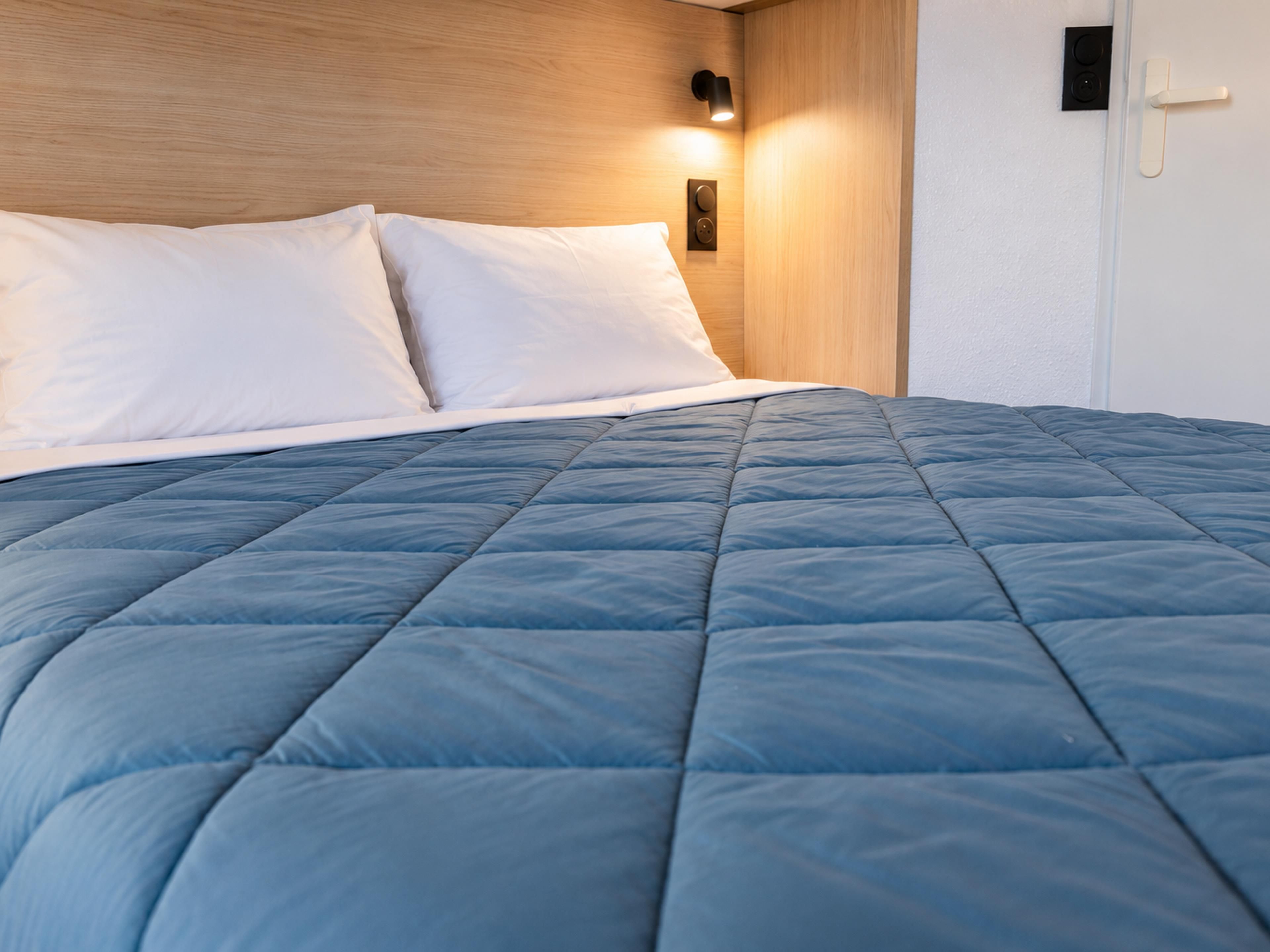 A bed with a blue quilt, white pillows, and a wooden headboard.