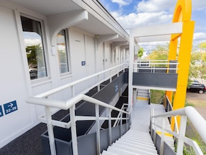 A staircase leading to a building with numbered rooms, a parking area, and a clear sky.