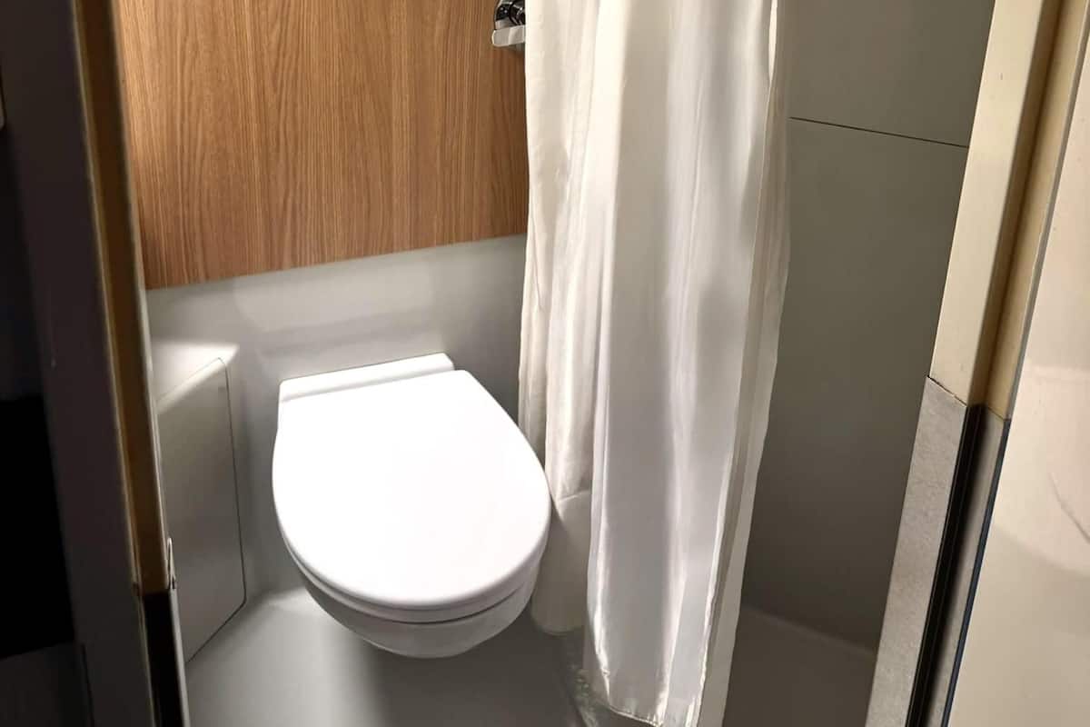 A small, compact bathroom with a white toilet, a wooden panel wall, and a white shower curtain.