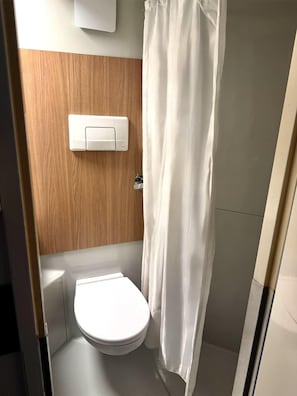 A small, compact bathroom with a white toilet, a wooden panel wall, and a white shower curtain.