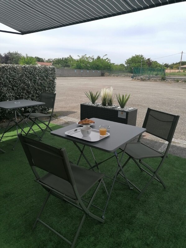 Un área de estar al aire libre con una mesa y sillas, una bandeja con un croissant, una taza y un vaso de jugo de naranja.