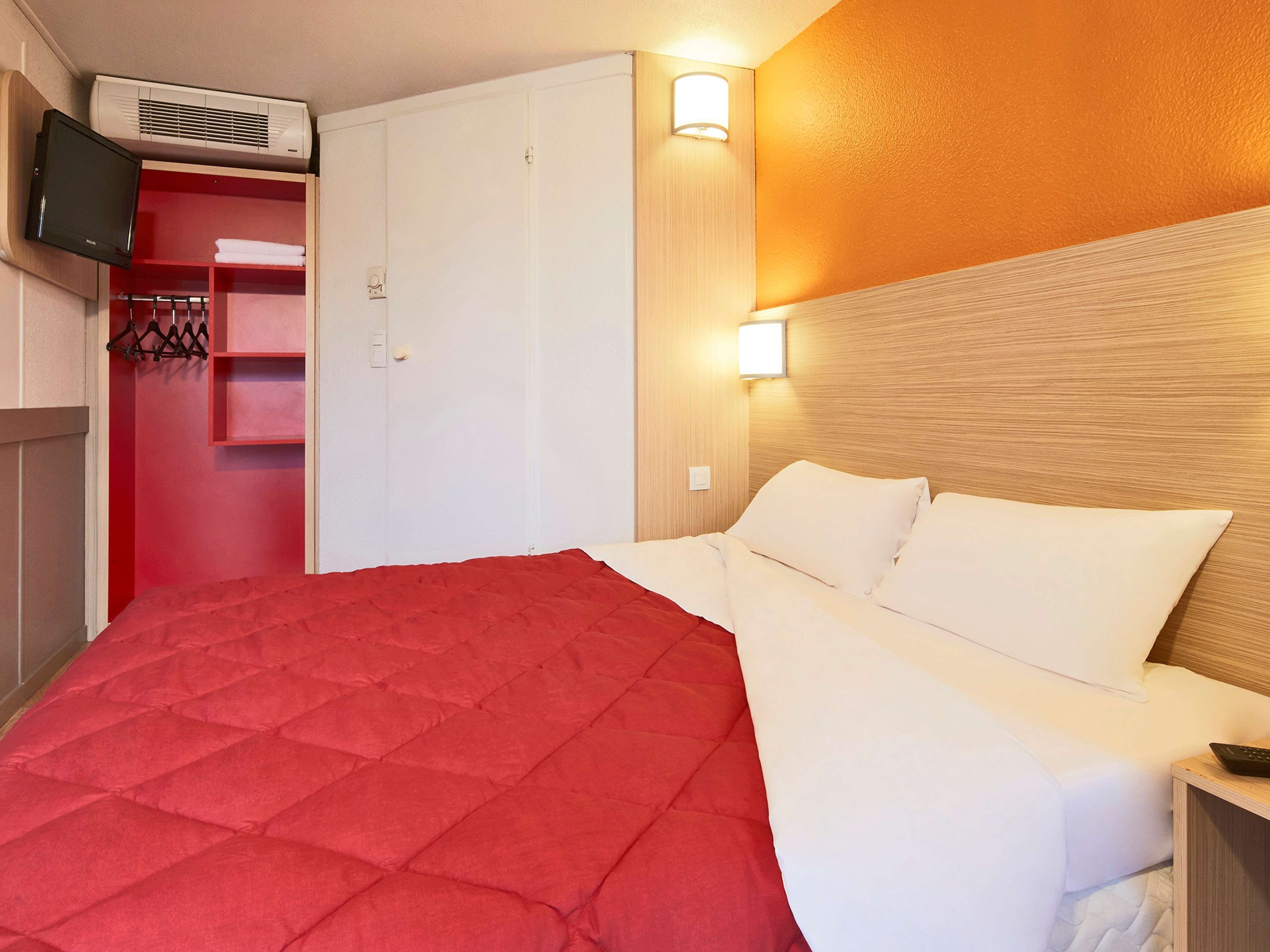 Una habitación de hotel con una cama, un televisor montado en la pared y un armario.