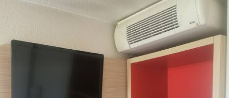 A room with a mounted flat-screen TV, a red shelving unit, and an air conditioning unit on the wall.