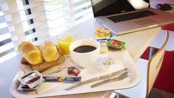 A breakfast tray with bread, juice, coffee, yogurt, and a laptop on a table.