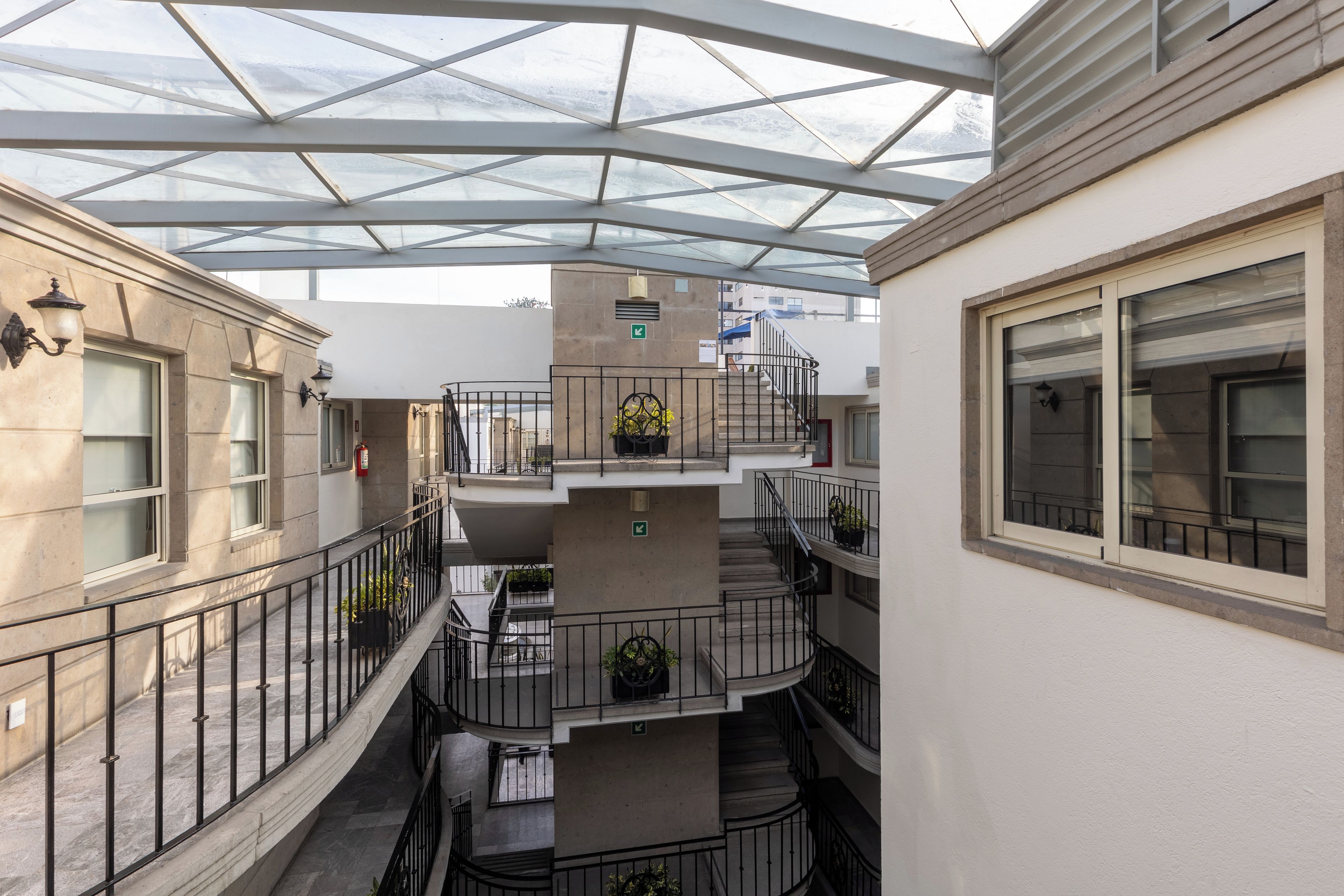 Un edificio de varios niveles con un atrio de cristal, mobiliario exterior y una escalera.