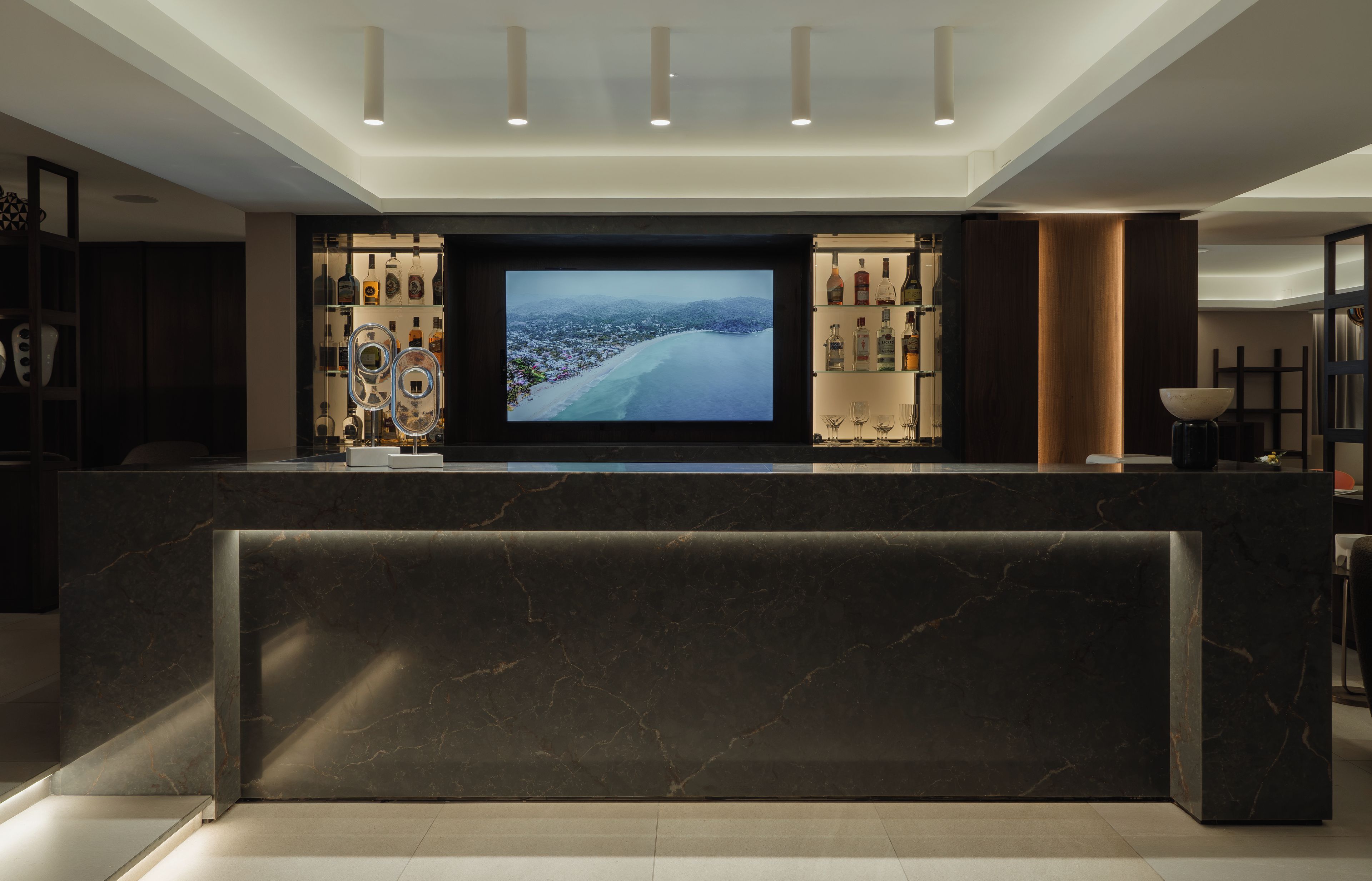 Un bar moderno con una televisión de pantalla plana grande, estantes llenos de botellas de licores y una encimera de mármol.