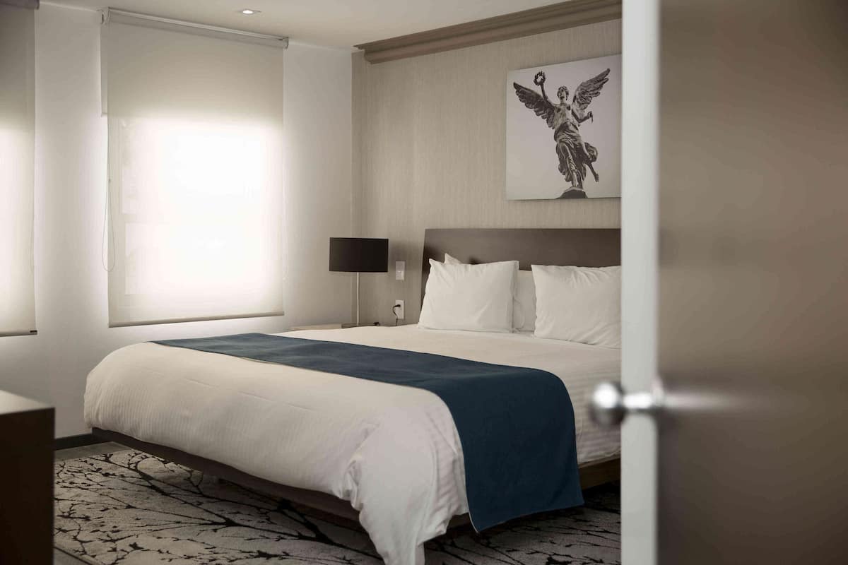 A hotel room with a large bed, a nightstand, a lamp, and a wall-mounted artwork.