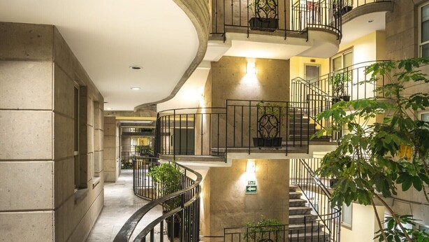 A multi-level interior with curved staircases, metal railings, and potted plants. - Suites Obelisk (Mexico City)