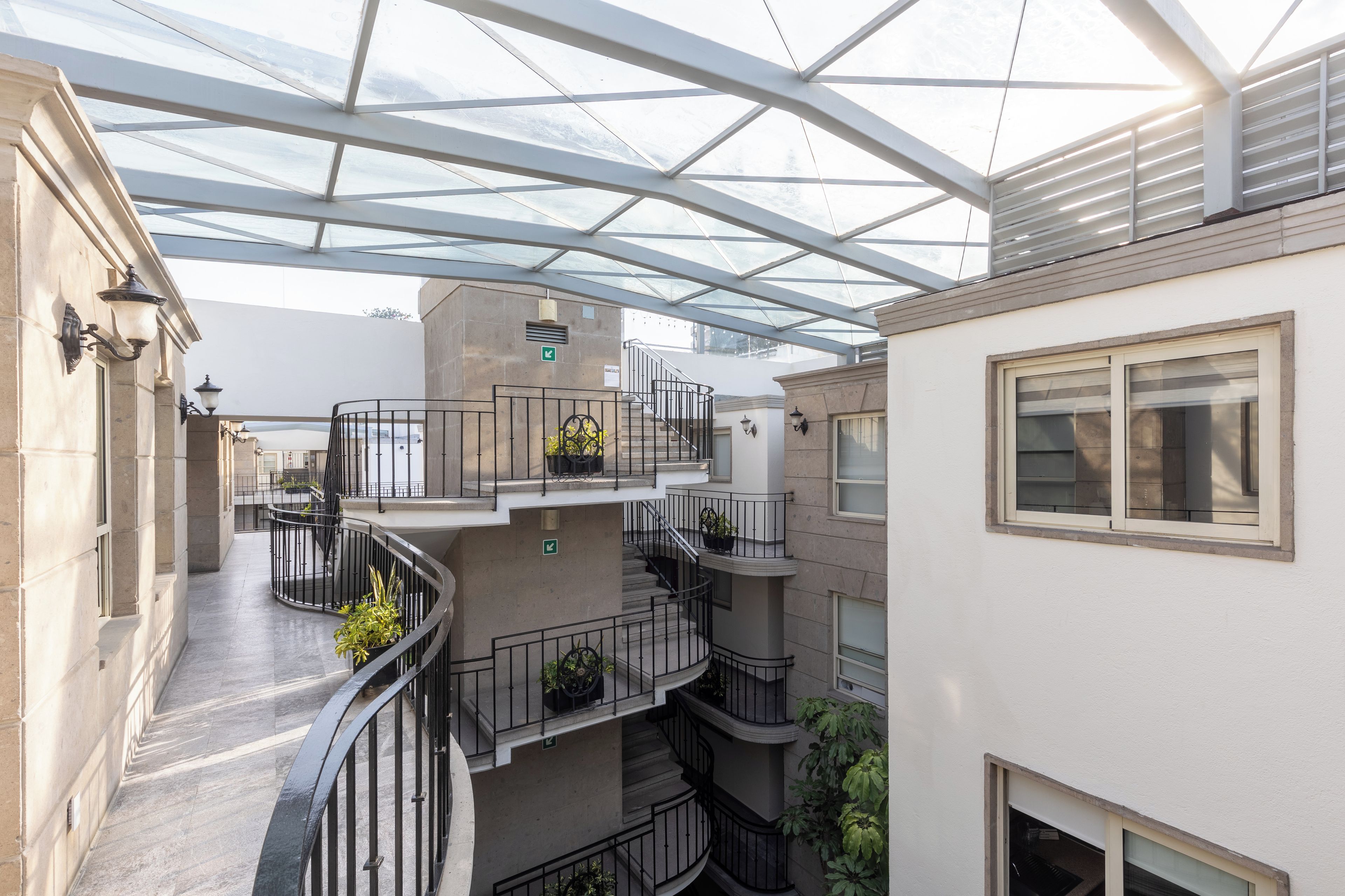 A multi-level building with a glass-enclosed atrium, outdoor staircases, and balconies with potted plants.