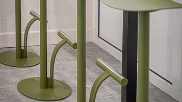 A series of green, modern, minimalist tables with curved legs and round tops, arranged in a row against a white wall with a dark column in the background.