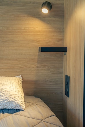 Una cama con un almohadón texturizado, un muro de madera y una lámpara en el techo.