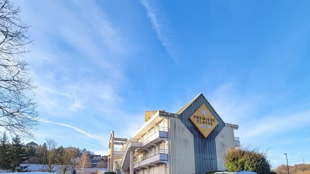 Un hotel con un llamativo letrero de 'Premiere Classe', un estacionamiento y un cielo azul despejado.