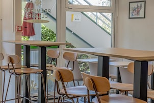 Interior de restaurante com mesas e cadeiras, vista de área externa através de uma janela, e um letreiro indicando o nome do restaurante.