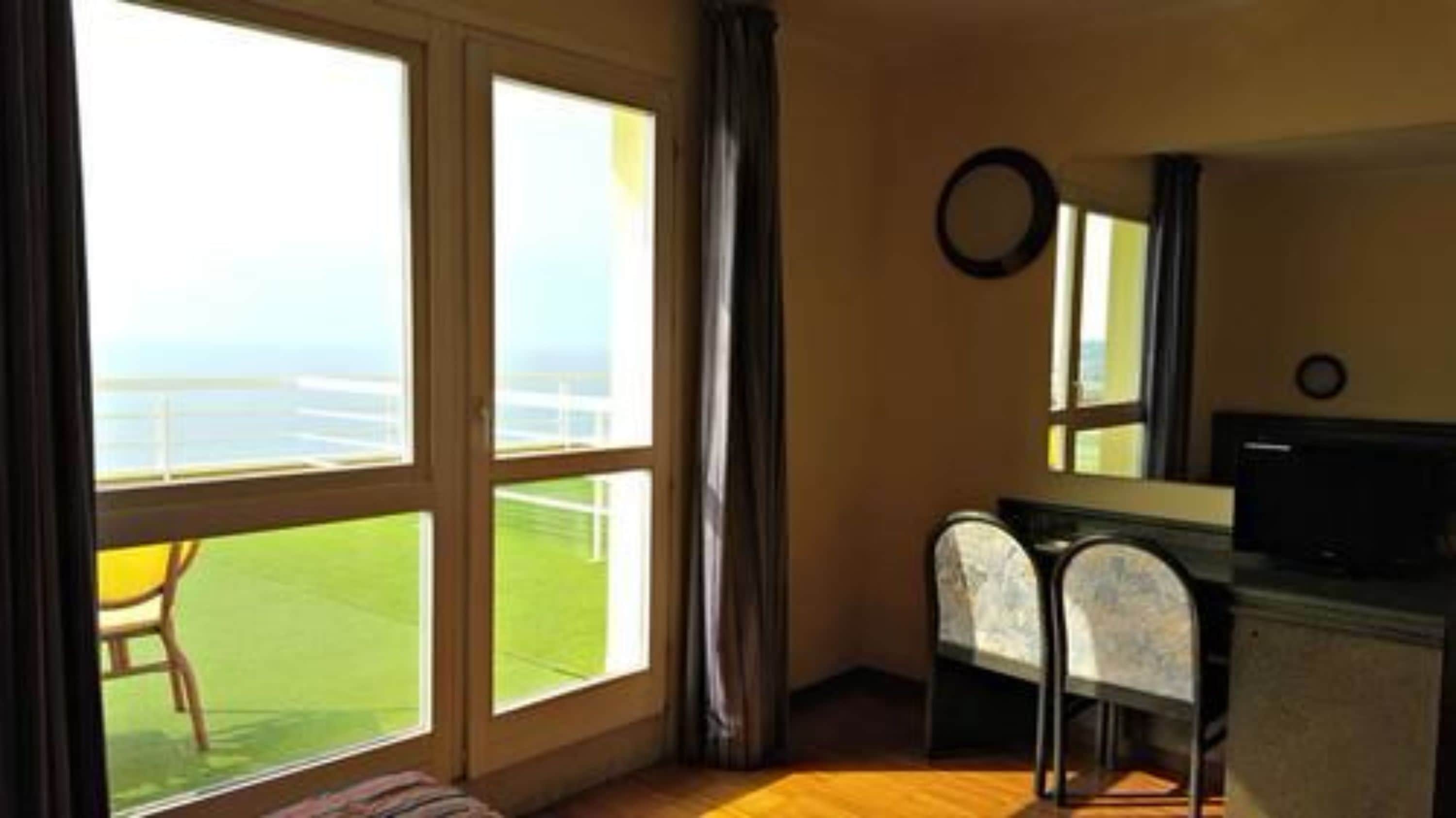 Une pièce avec une grande fenêtre, une chaise, un bureau et un miroir.
