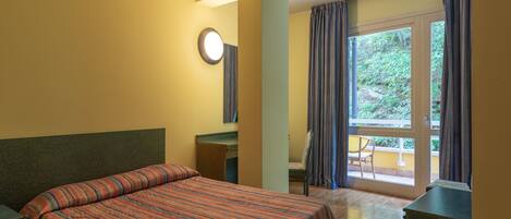Una habitación de hotel con cama, escritorio, silla y ventana con cortinas.