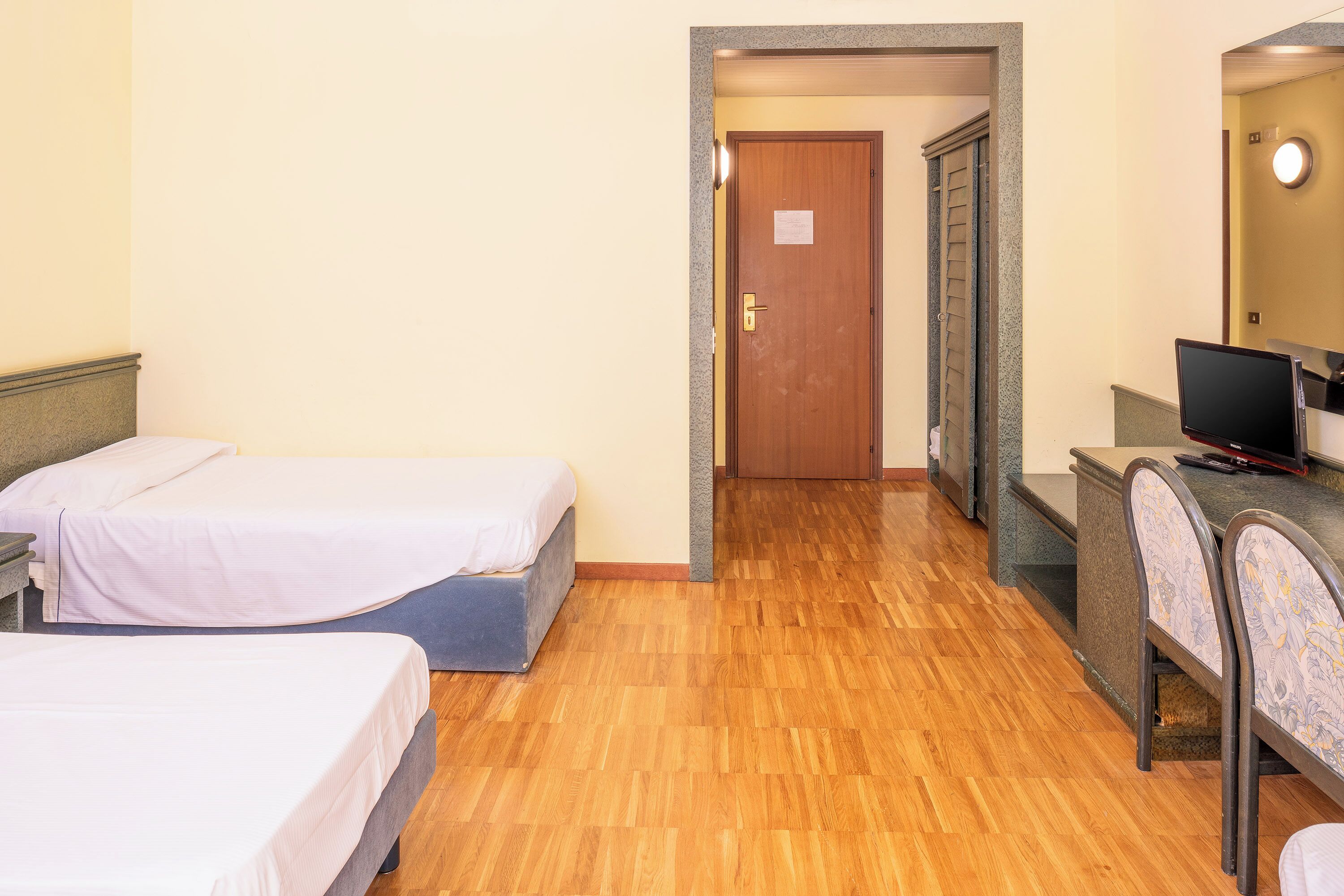 A hotel room with two single beds, a desk with a computer, and a bathroom door.