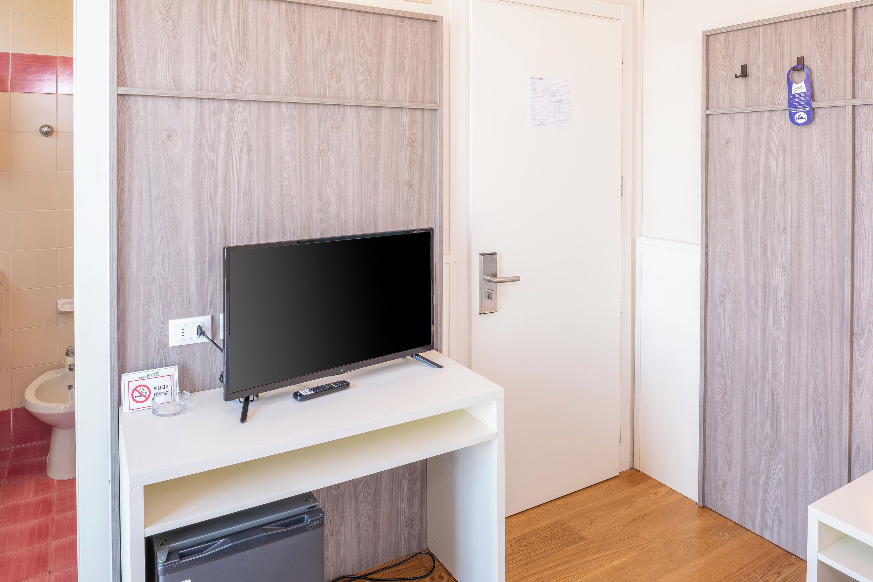 A bathroom with a toilet, a sink, a mirror, and a television on a white stand.